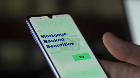 Photo for An investor analyzing the mortgage-backed securities etf fund on a screen. A phone shows the prices of Mortgage-Backed Securities - Royalty Free Image
