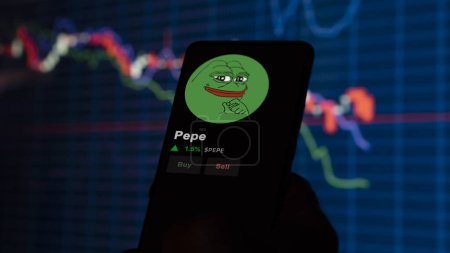 Foto de 24 de noviembre de 2023. Un inversor analizando el precio de Pepe en un teléfono, la moneda simbólica $PEPE en un intercambio criptográfico sreen. - Imagen libre de derechos