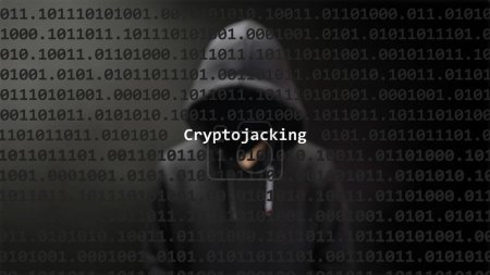 Ciberataque cryptojacking texto en pantalla de primer plano, hacker anónimo oculto con sudadera con capucha en el fondo borroso. Texto de vulnerabilidad en código binario del sistema en el programa editor.