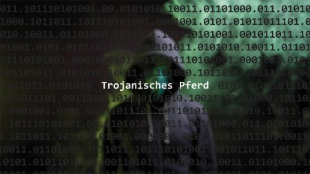 Cyber attack. Translation: trojan horse text in foreground screen, anonymous hacker hidden with hoodie in the blurred background. Vulnerability text in binary system code on editor program.