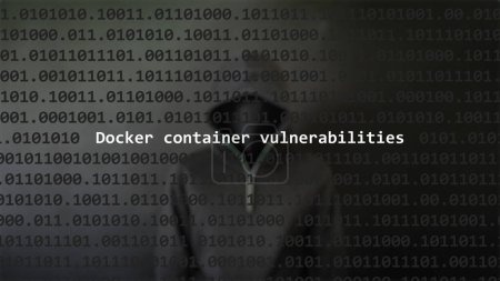Cyber attack docker container vulnerabilities text in foreground screen, anonymous hacker hidden with hoodie in the blurred background. Vulnerability text in binary system code on editor program.