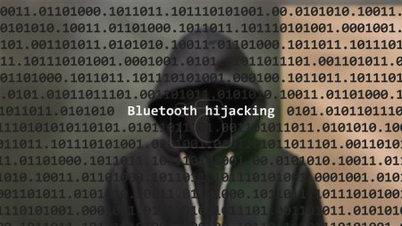 Cyber attack bluetooth hijacking text in foreground screen, anonymous hacker hidden with hoodie in the blurred background. Vulnerability text in binary system code on editor program.