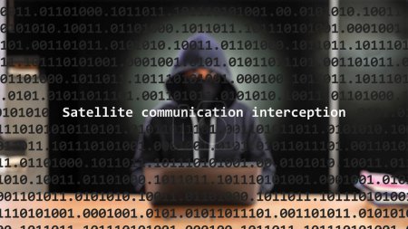 Cyber attack satellite communication interception text in foreground screen, anonymous hacker hidden with hoodie in the blurred background. Vulnerability text in binary system code on editor program.