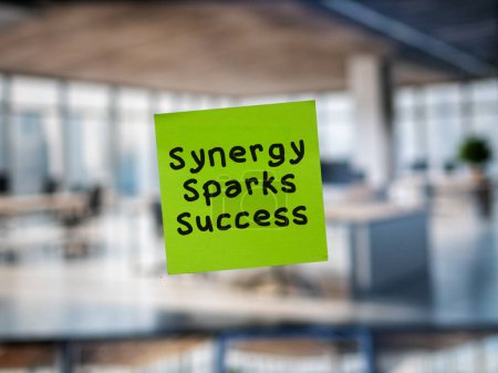 Post note on glass with 'Synergy Sparks Success'.