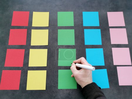 Hand writing on a colorful array of sticky notes on a grey background.