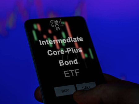 An investor analyzing the intermediate core-plus bond etf fund on a screen. A phone shows the prices of Intermediate Core-Plus Bond