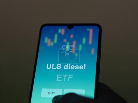 Photo for An investor analyzing the uls diesel etf fund on a screen. A phone shows the prices of ULS diesel - Royalty Free Image