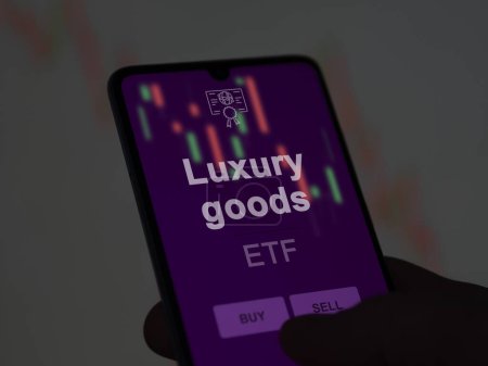 An investor analyzing the luxury goods etf fund on a screen. A phone shows the prices of Luxury goods