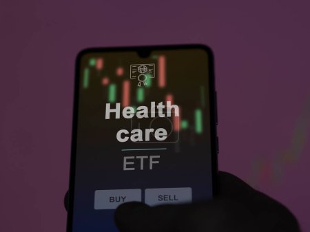 An investor analyzing the health care etf fund on a screen. A phone shows the prices of Health care