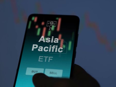 An investor analyzing the asia pacific etf fund on a screen. A phone shows the prices of Asia Pacific
