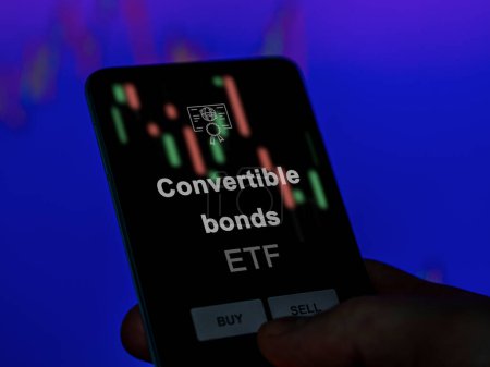 Un inversor analizando los bonos convertibles etf fondo en una pantalla. Un teléfono muestra los precios de los bonos convertibles