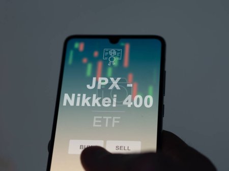 An investor analyzing the jpx - nikkei 400 etf fund on a screen. A phone shows the prices of JPX - Nikkei 400