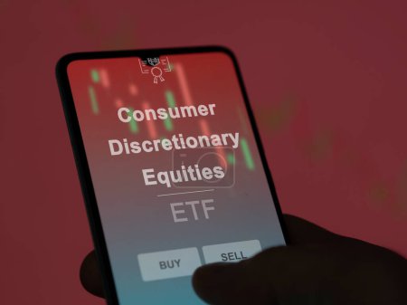 An investor analyzing the consumer discretionary equities etf fund on a screen. A phone shows the prices of Consumer Discretionary Equities