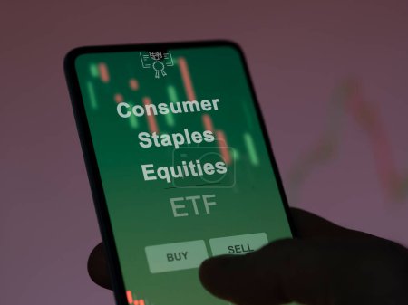 Ein Anleger analysiert auf einem Bildschirm die Konsumentenaktien und Fonds. Ein Telefon zeigt die Preise von Consumer Staples Aktien