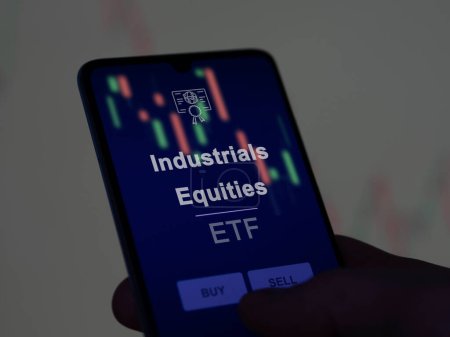 An investor analyzing the industrials equities etf fund on a screen. A phone shows the prices of Industrials Equities
