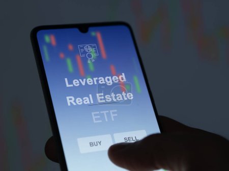 An investor analyzing the leveraged real estate etf fund on a screen. A phone shows the prices of Leveraged Real Estate