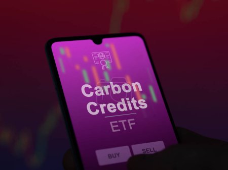 An investor analyzing the carbon credits etf fund on a screen. A phone shows the prices of Carbon Credits