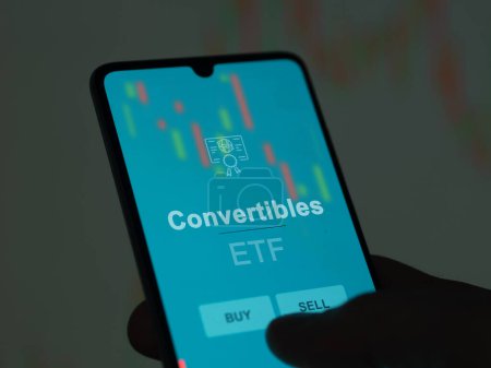 An investor analyzing the convertibles etf fund on a screen. A phone shows the prices of Convertibles