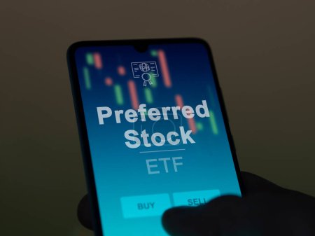 An investor analyzing the preferred stock etf fund on a screen. A phone shows the prices of Preferred Stock