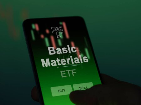 An investor analyzing the basic materials etf fund on a screen. A phone shows the prices of Basic Materials