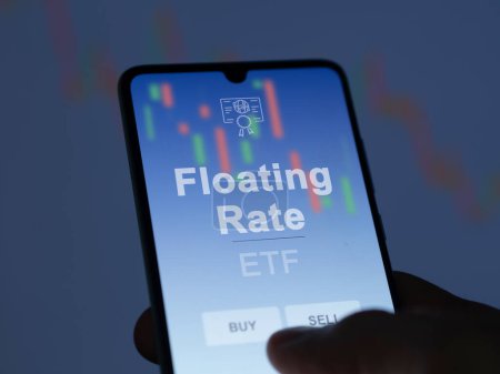 An investor analyzing the floating rate etf fund on a screen. A phone shows the prices of Floating Rate