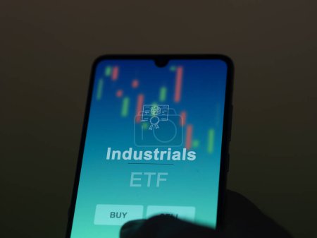An investor analyzing the industrials etf fund on a screen. A phone shows the prices of Industrials