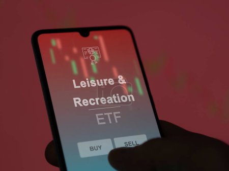An investor analyzing the leisure & recreation etf fund on a screen. A phone shows the prices of Leisure & Recreation