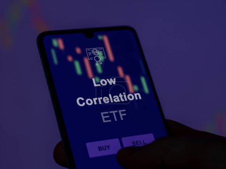 Photo for An investor analyzing the low correlation etf fund on a screen. A phone shows the prices of Low Correlation - Royalty Free Image