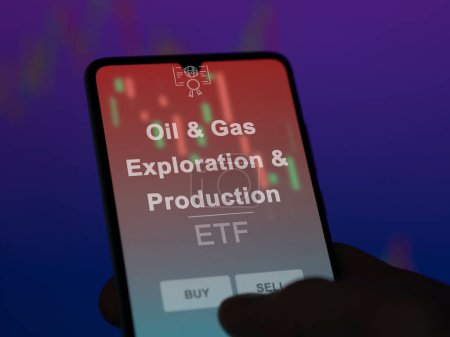 An investor analyzing the oil & gas exploration & production etf fund on a screen. A phone shows the prices of Oil & Gas Exploration & Production