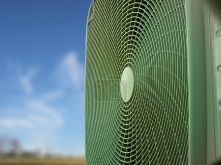 Green heat pump on foreground, blurred sly and trees in the background, short lens.