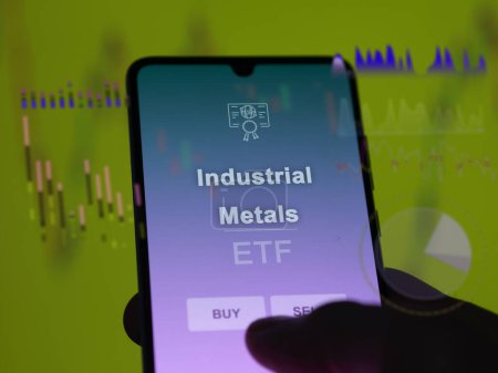 An investor analyzing the industrial metals etf fund on a screen. A phone shows the prices of Industrial Metals