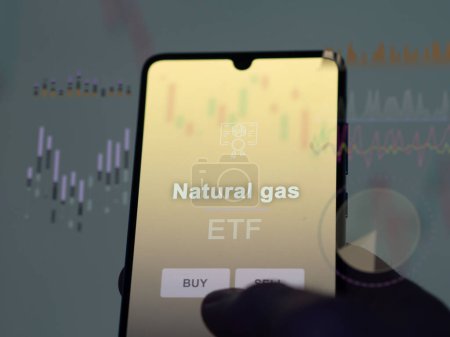 An investor analyzing the natural gas etf fund on a screen. A phone shows the prices of Natural gas