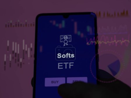 Un inversor analizando el fondo etf blandos en una pantalla. Un teléfono muestra los precios de Softs