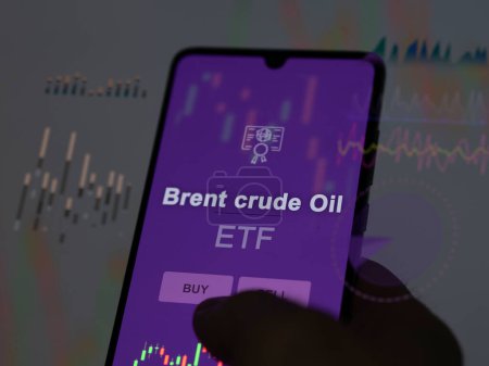 An investor analyzing the brent crude oil etf fund on a screen. A phone shows the prices of Brent crude Oil