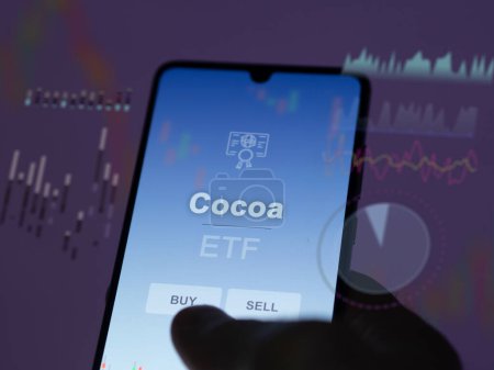Un inversor analizando el fondo de cacao etf en una pantalla. Un teléfono muestra los precios de Cacao