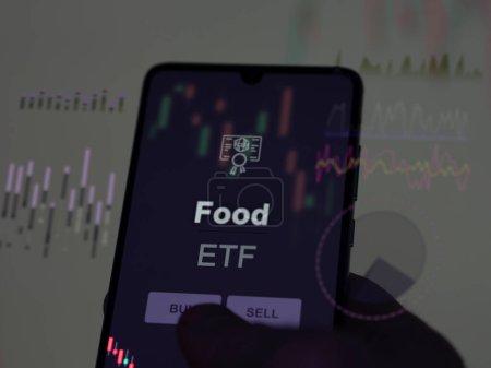 An investor analyzing the food etf fund on a screen. A phone shows the prices of Food