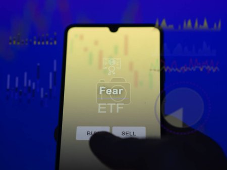 An investor analyzing the fear etf fund on a screen. A phone shows the prices of Fear