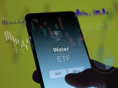 An investor analyzing the water etf fund on a screen. A phone shows the prices of Water