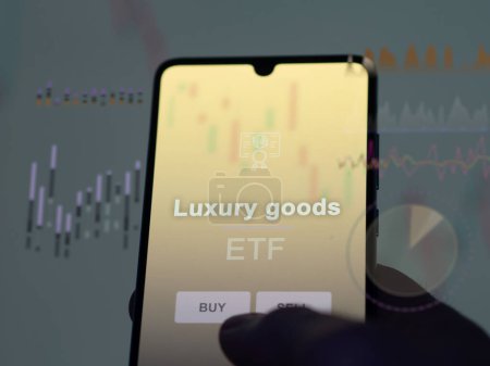 An investor analyzing the luxury goods etf fund on a screen. A phone shows the prices of Luxury goods