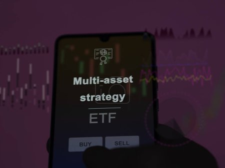 An investor analyzing the multi-asset strategy etf fund on a screen. A phone shows the prices of Multi-asset strategy
