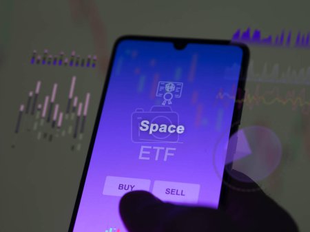 Un inversor analizando el fondo de espacio etf en una pantalla. Un teléfono muestra los precios del Espacio