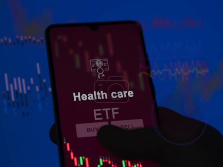 An investor analyzing the health care etf fund on a screen. A phone shows the prices of Health care