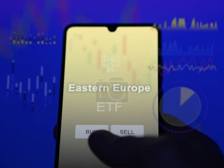 Téléchargez les photos : Un investisseur qui analyse le fonds de l'Europe de l'Est sur un écran. Un téléphone montre les prix de l'Europe de l'Est - en image libre de droit