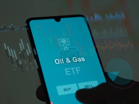 Téléchargez les photos : Un investisseur analyse le fonds pétrolier et gazier etf sur un écran. Un téléphone affiche les prix du pétrole et du gaz - en image libre de droit