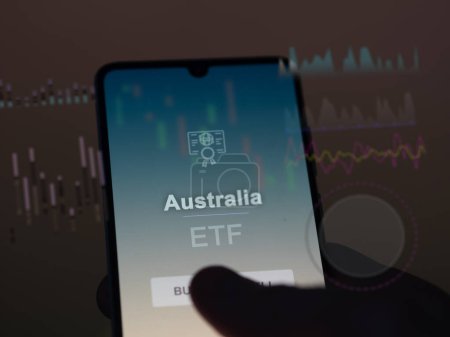 An investor analyzing the australia etf fund on a screen. A phone shows the prices of Australia