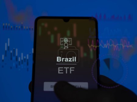 An investor analyzing the brazil etf fund on a screen. A phone shows the prices of Brazil
