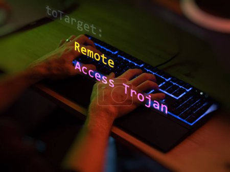 Cyber attack remote access trojan text in foreground screen, hands of a anonymous hacker on a led keyboard. Vulnerability text in informatic system style, code on editor screen. Text in English, English text