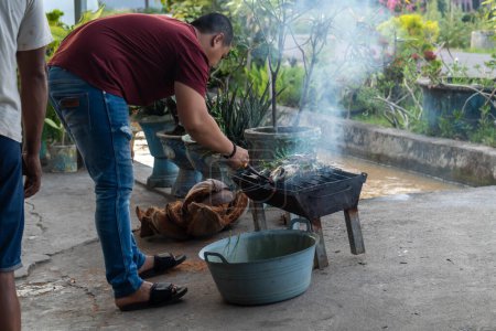 Téléchargez les photos : Pinrang Indonésie, 05 décembre 2023 : quelqu'un fait griller du poisson l'après-midi pendant la saison des pluies Lieu de grillage du poisson en charbon de bois et ceinture de noix de coco, Asie Indonésie, - en image libre de droit