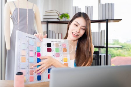 Photo for Asian female clothing designers Thailand communicating with customers through laptops in their home office. Showing various color patterns for customers to choose from cut dress as the customer wants. - Royalty Free Image