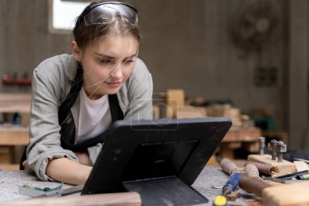 Photo for Portrait of a female carpenter looking at designs on a tablet for making her furniture in a furniture factory. with many tools and wood - Royalty Free Image